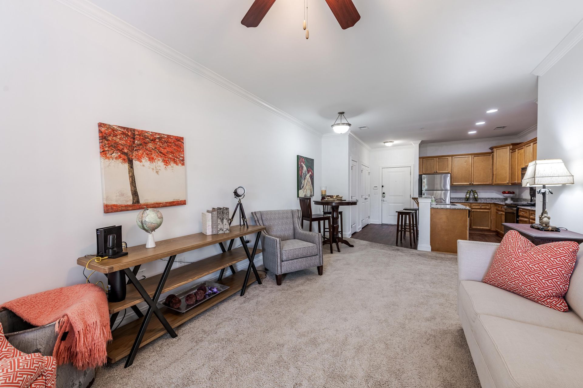 Living room with open kitchen. Beige carpet, white walls, and wood-toned furniture at Plantation at Pleasant Ridge in Greensboro, NC.