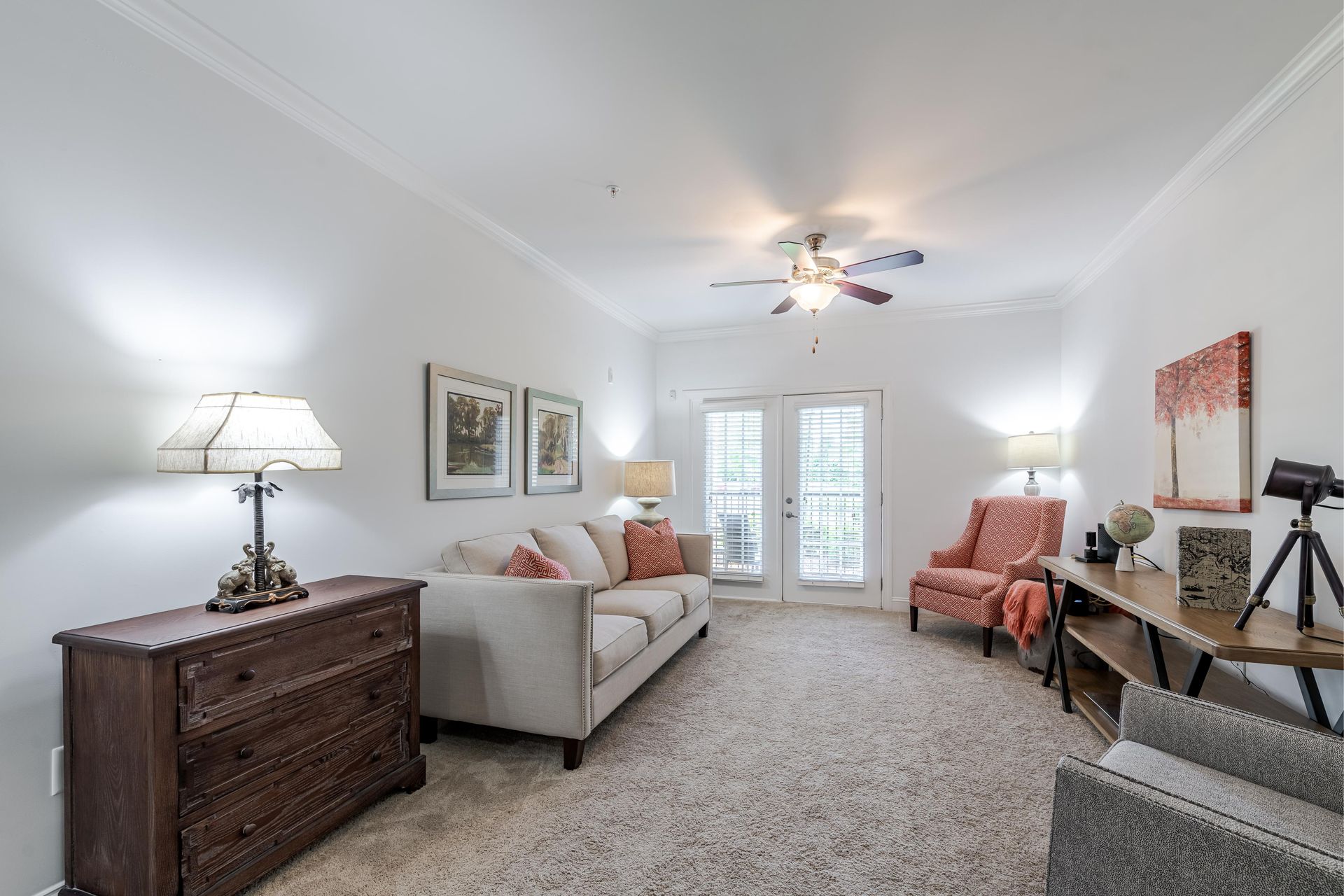 Living room with cream-colored sofa, two armchairs, a wooden dresser, and a door leading to a balcony at Plantation at Pleasant Ridge in Greensboro, NC.
