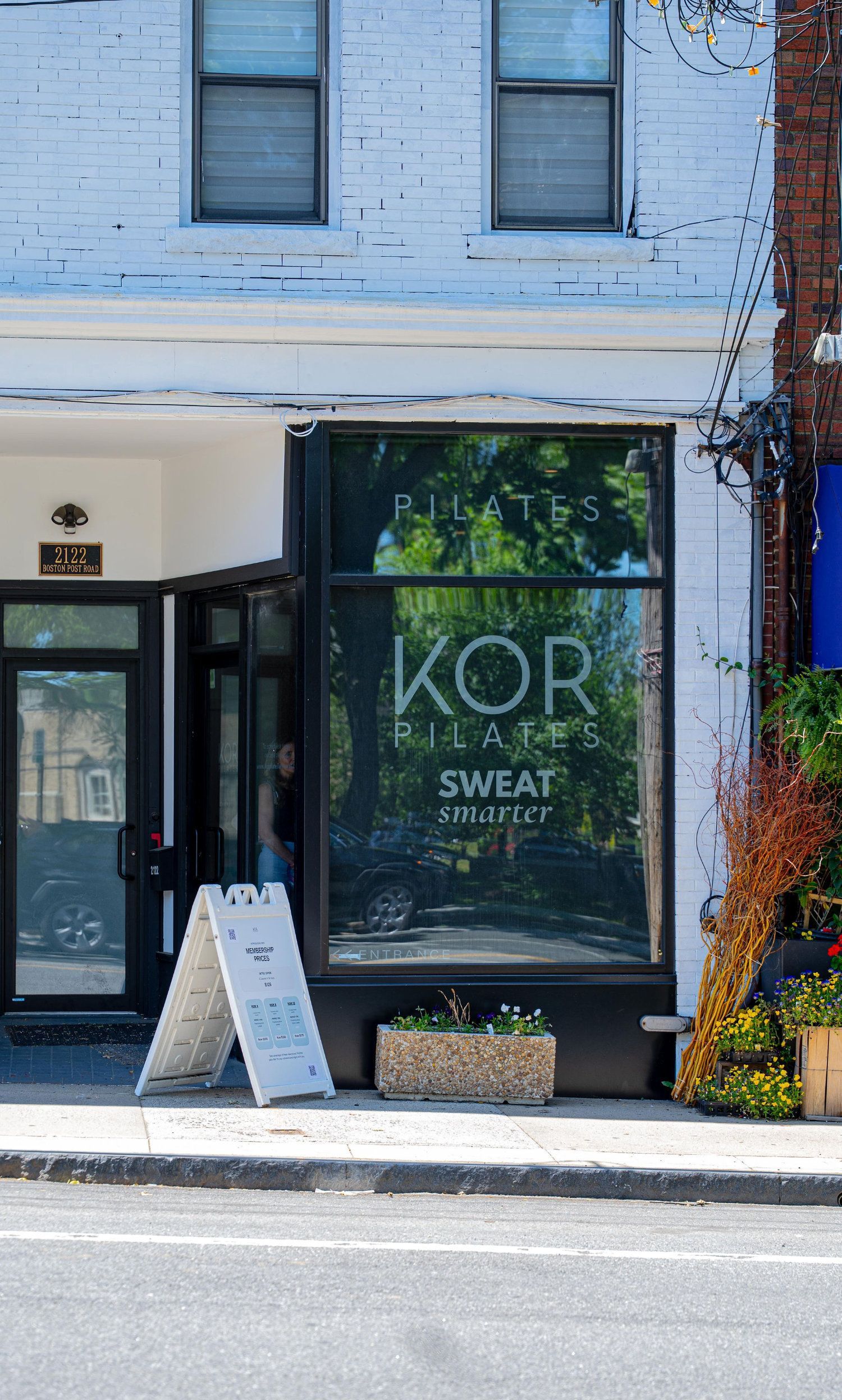 Storefront with large window sign reading “KORI SWEET,” white facade, and sidewalk sandwich board sign.