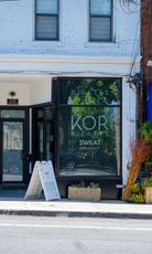 Storefront with large window sign reading “KORI SWEET,” white facade, and sidewalk sandwich board sign.
