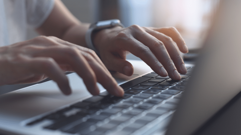 Person typing on a laptop keyboard with both hands, wearing a smartwatch.