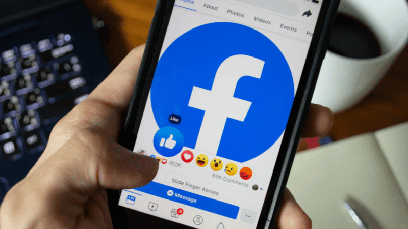Person holding phone displaying Facebook app; reacting to a post with a like.