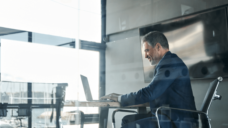 Man in suit working on laptop at a desk in a modern office, looking focused.