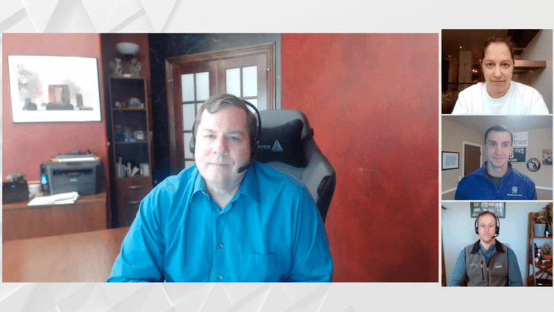 Panel of four men on a video call; one man in a blue shirt is centered, others in smaller windows.