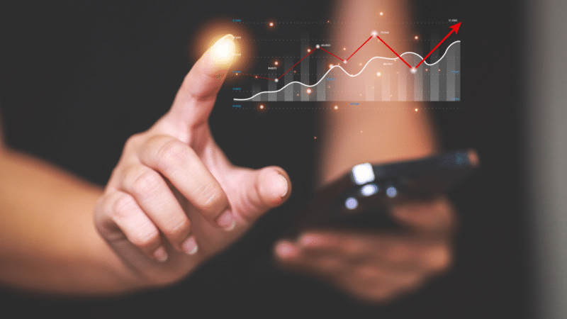 Person using smartphone, finger pointing to a glowing graph with a red upward trend, symbolizing financial growth.