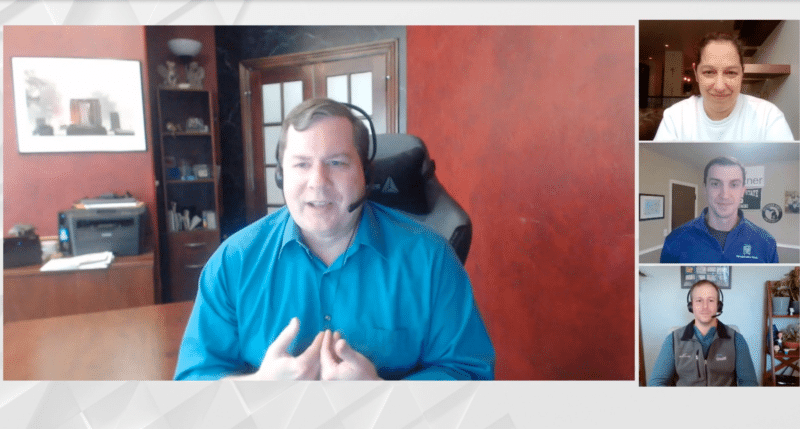 Panel of four men on a video call, discussing something, with the main speaker wearing a blue shirt and headset.