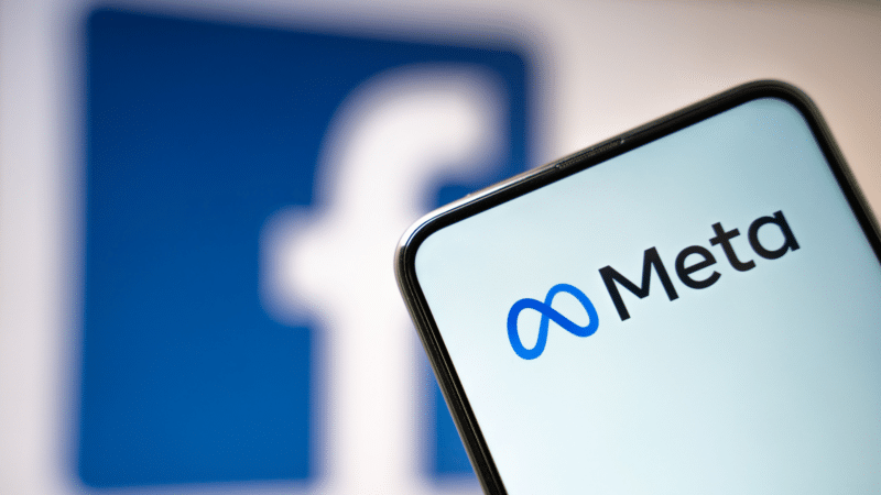 Smartphone displaying the Meta logo in front of a Facebook logo in the background.
