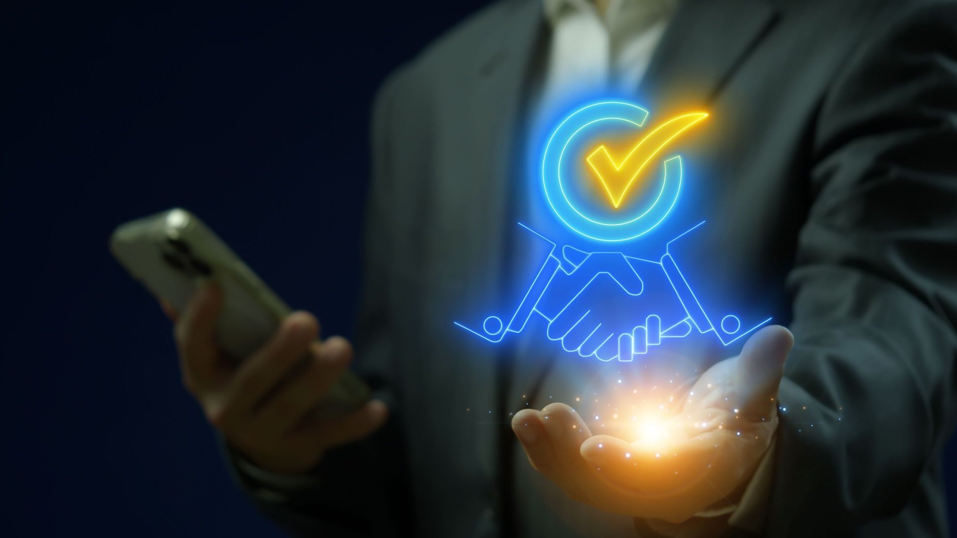 Person in a suit holding a glowing hologram of two hands shaking with a checkmark above.