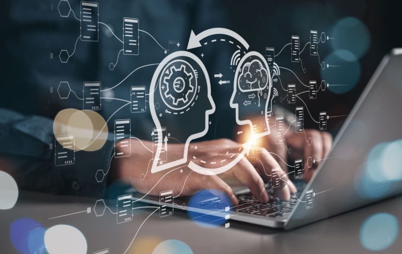 Person typing on laptop with overlay of two head silhouettes exchanging data, with bokeh.