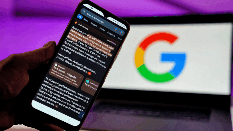 A hand holding a phone displaying a news article, Google logo in the background.