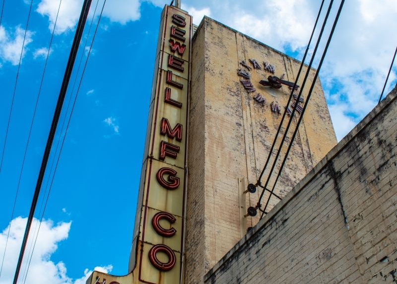 Tall, weathered sign for the Sewell Coco theater with a clock face.