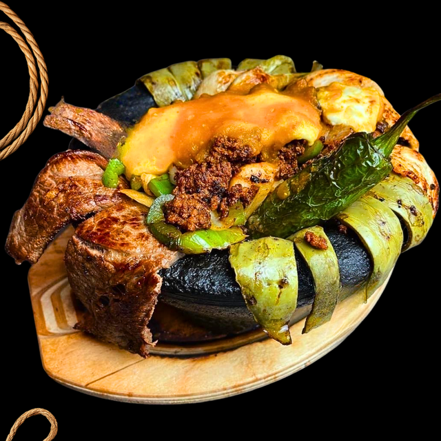 Grilled meat and vegetables in a sizzling pot on a wooden board. Black background.