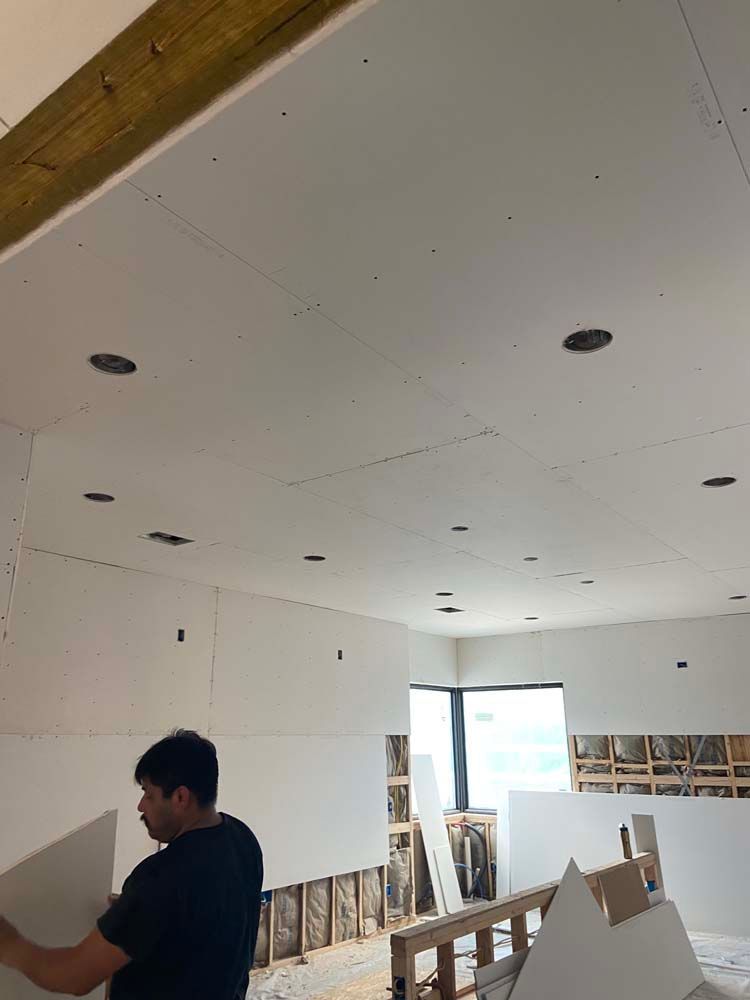 Man installing drywall on a ceiling with recessed lighting. Interior view of a room under construction.
