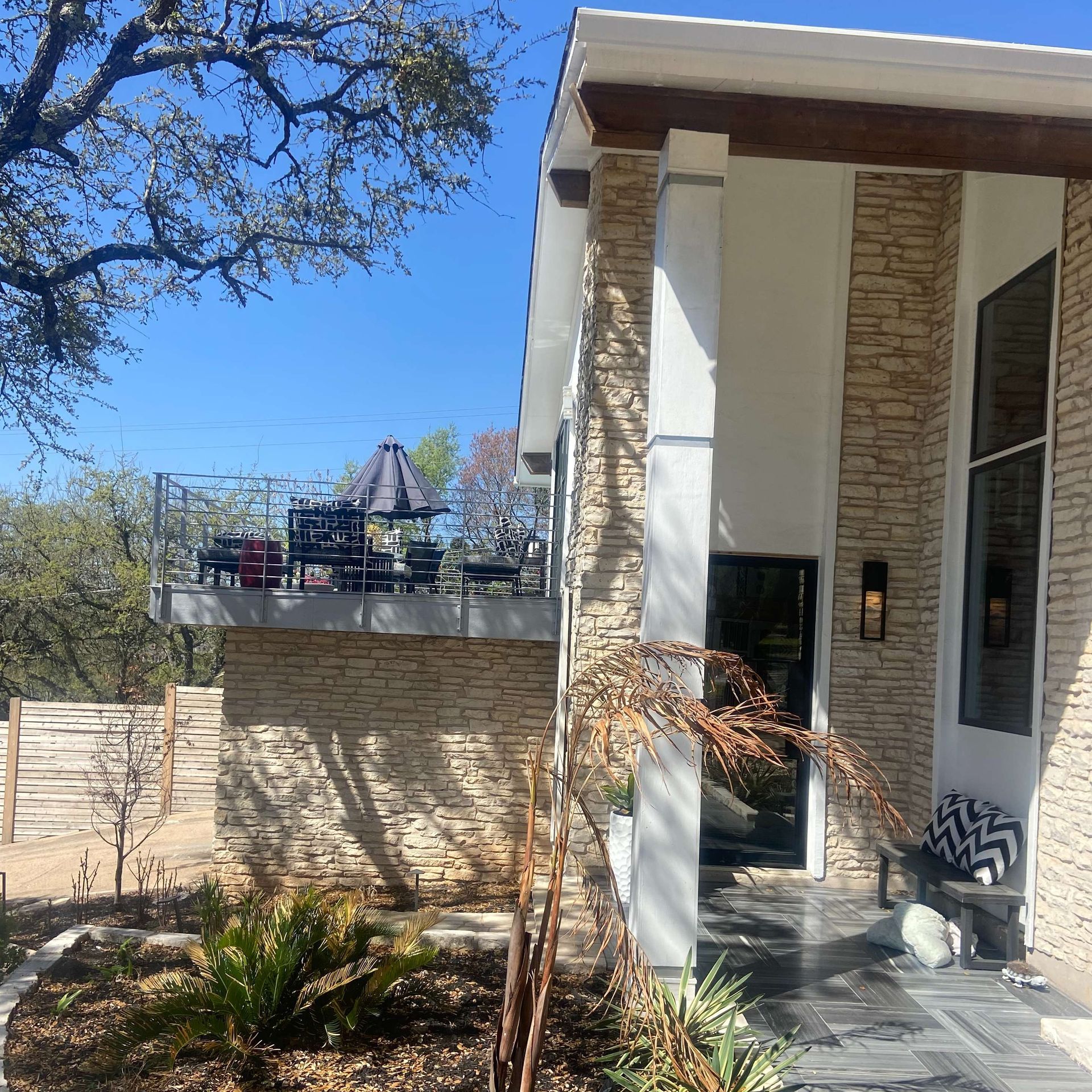 Modern house with a stone exterior, balcony, and outdoor seating on a sunny day.