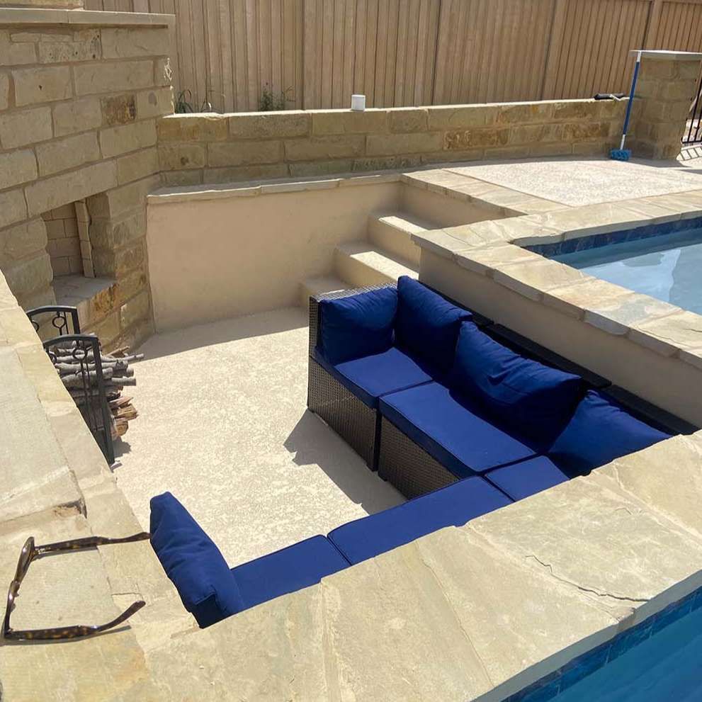 Blue sectional seating in a sunken patio area beside a pool. Tan stone walls and steps.