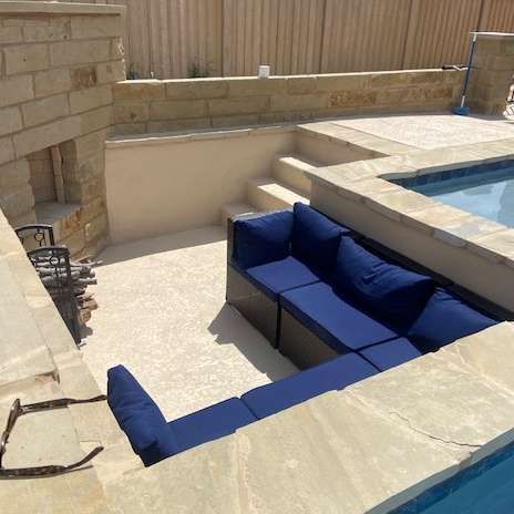 L-shaped blue outdoor sofa by a pool with a stone surround and a built-in fireplace.