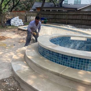 Man working on the edge of a pool. Tan stone steps lead to the blue tiled pool. Outdoors, daytime.