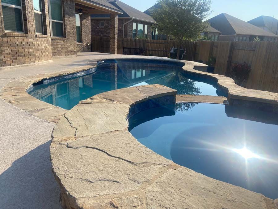 Swimming pool with stone edging and blue water, surrounded by patio and house.