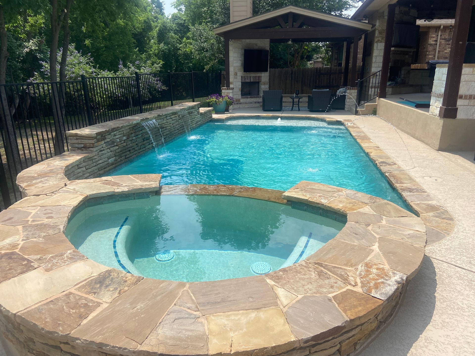 Swimming pool with a connected spa, waterfall feature, and outdoor kitchen.