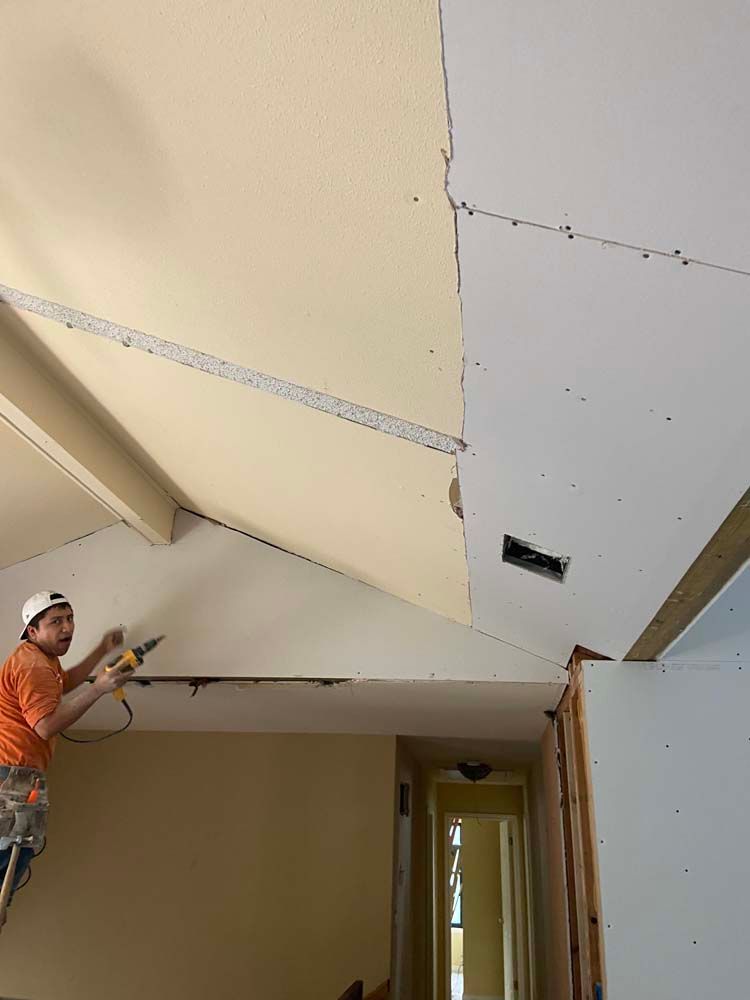 A person on a ladder installing drywall on an angled ceiling, interior setting.