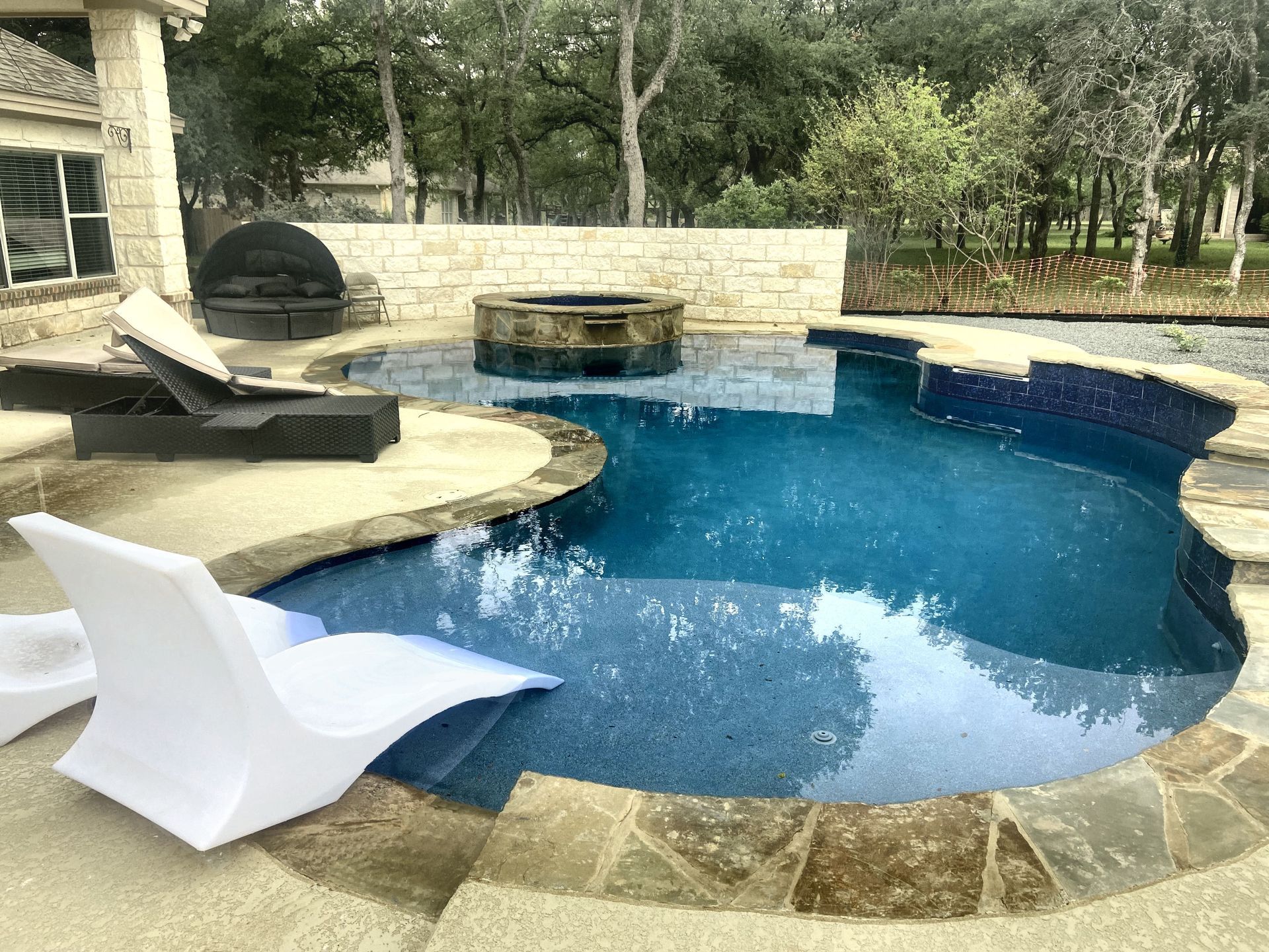 Swimming pool with blue tile, stone coping, and white lounge chairs.