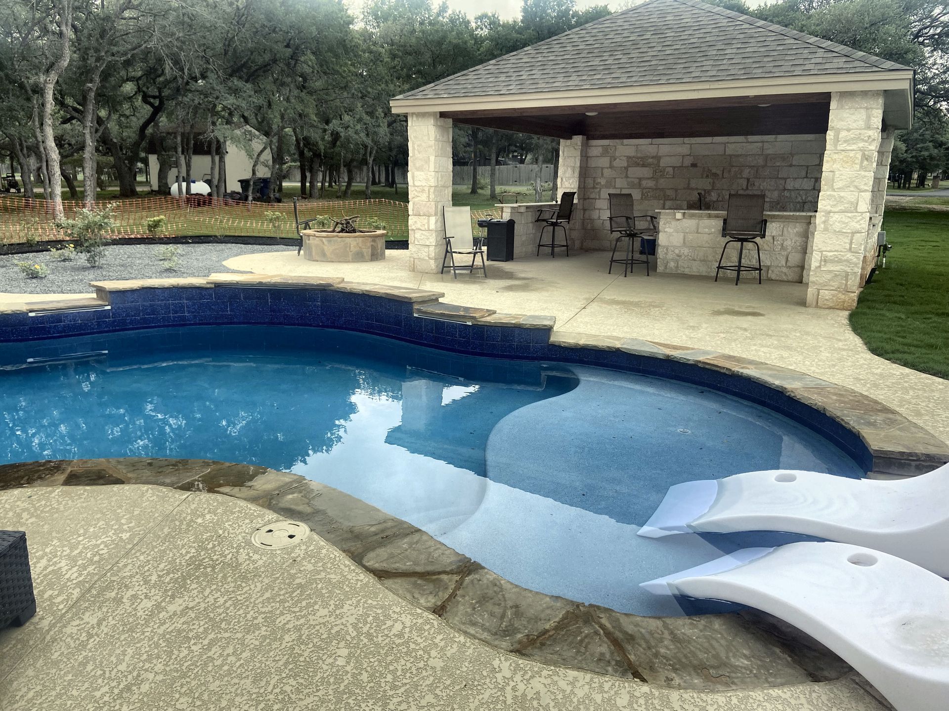 Pool with blue water and a stone-covered gazebo with bar seating.