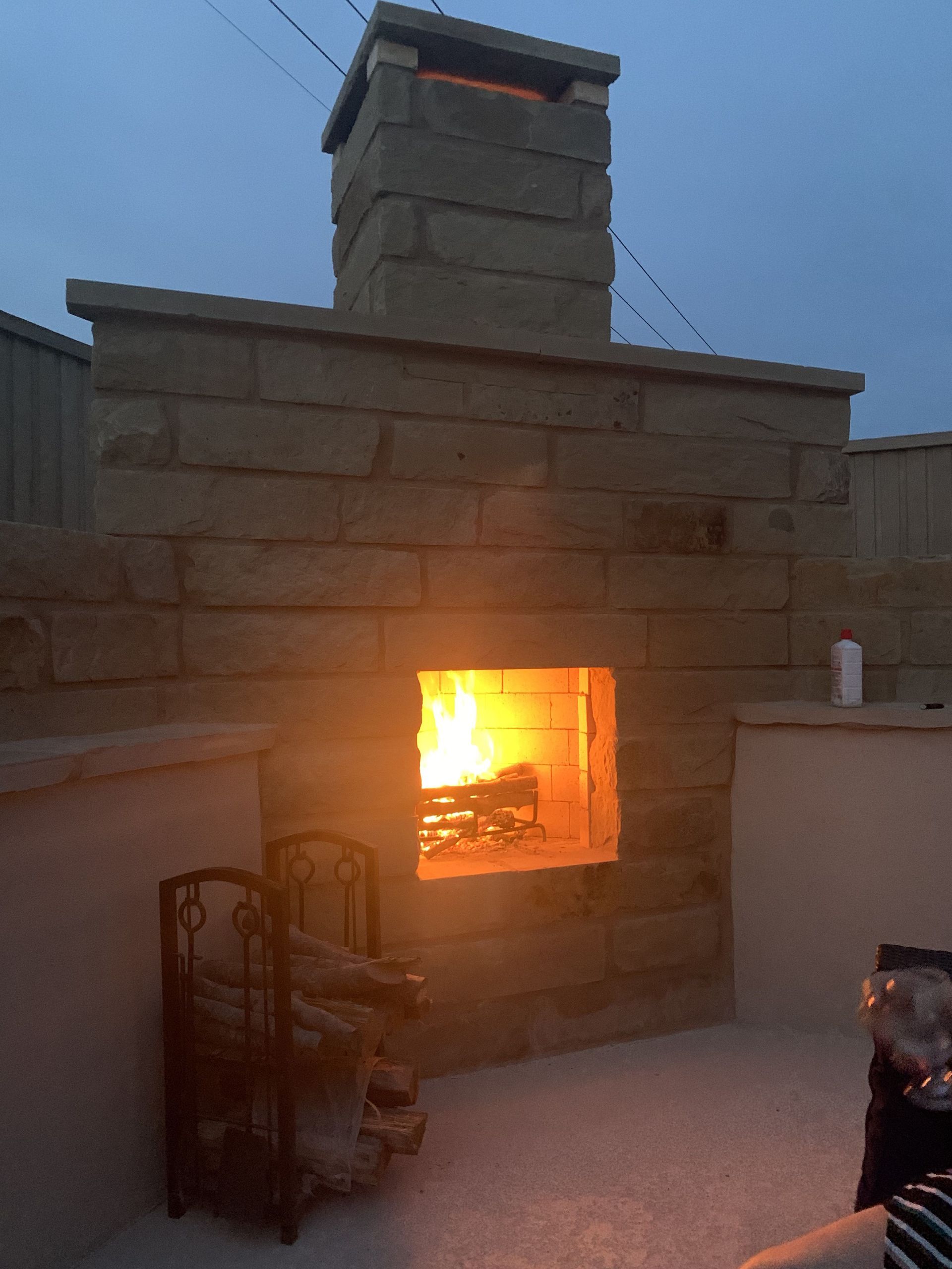 Fireplace with burning flames outdoors at dusk, built of stone blocks.