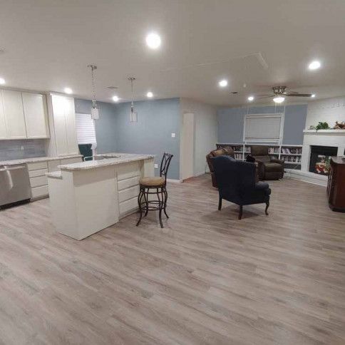 Open-concept kitchen and living area with light wood floors, white cabinets, blue-gray walls, and a fireplace.