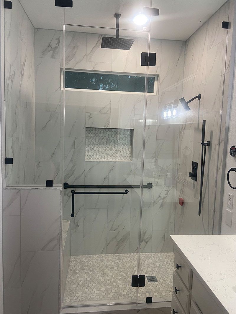 Modern shower with marble-like tile, glass walls, and black hardware; includes a grab bar and shower head.