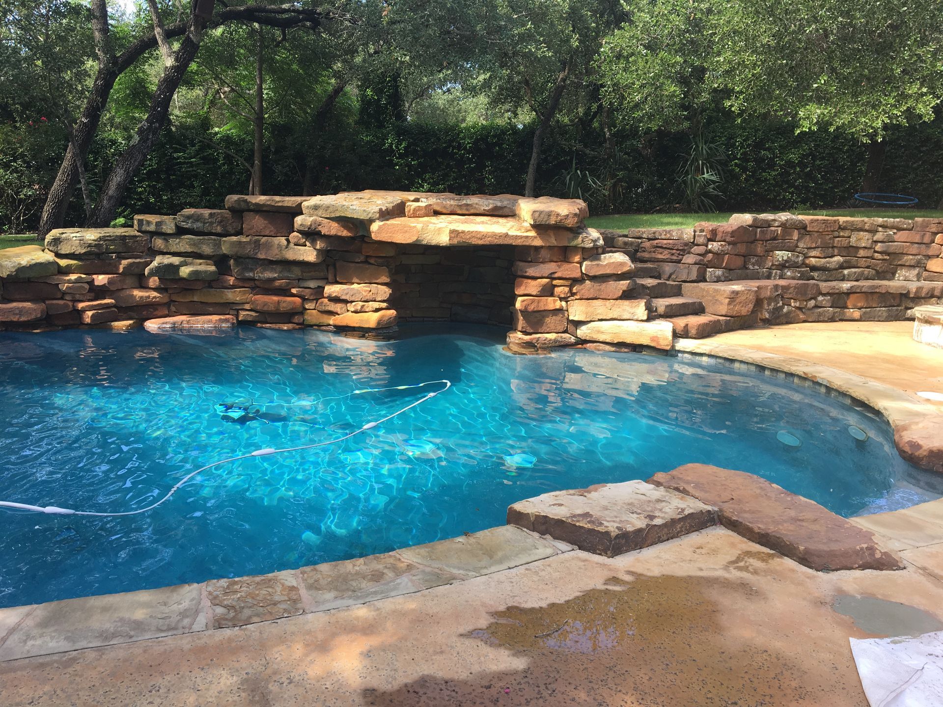 A swimming pool with a rock waterfall, turquoise water, and stone steps.