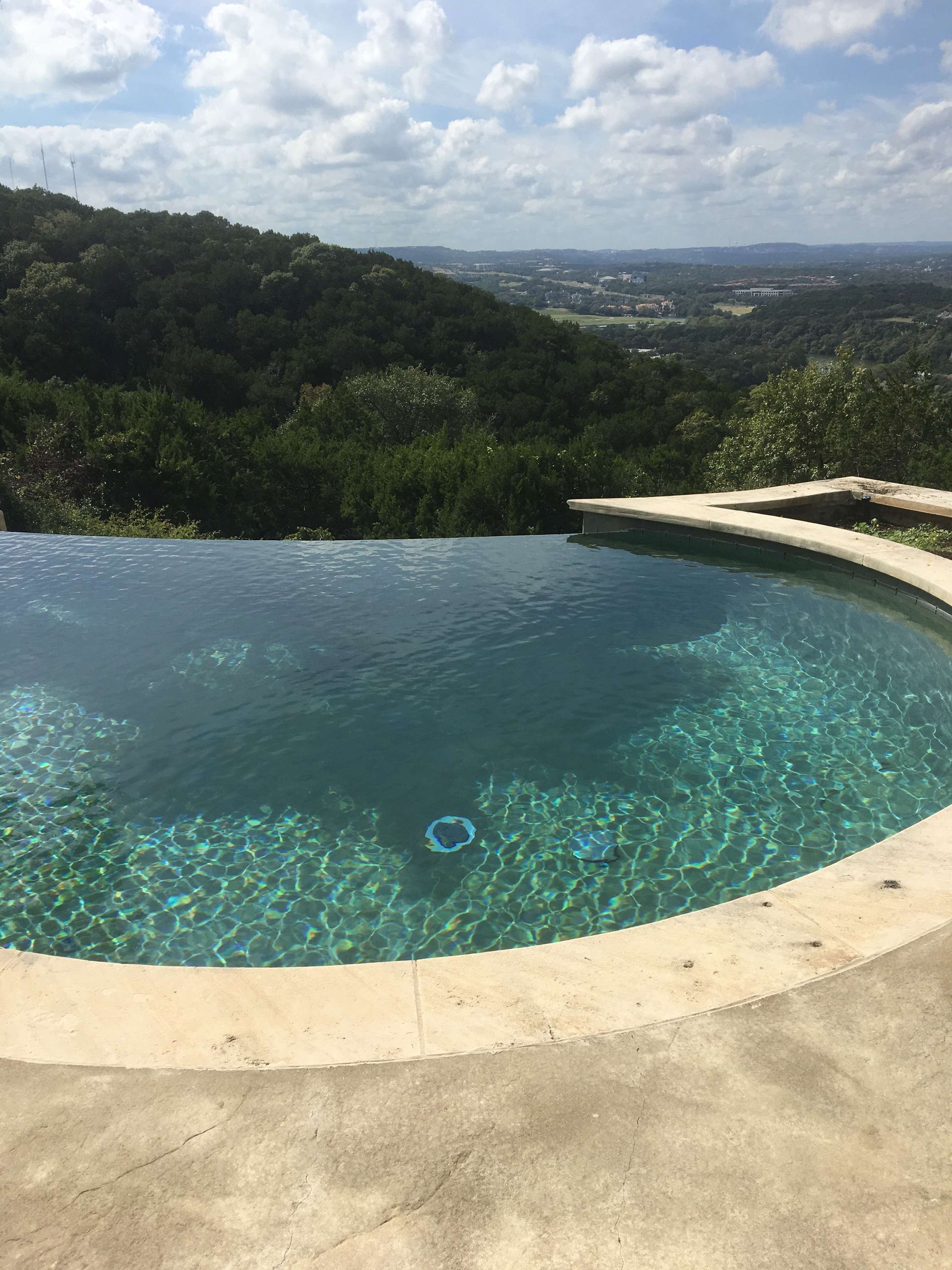 Infinity pool overlooking a valley with blue water and a natural stone deck.
