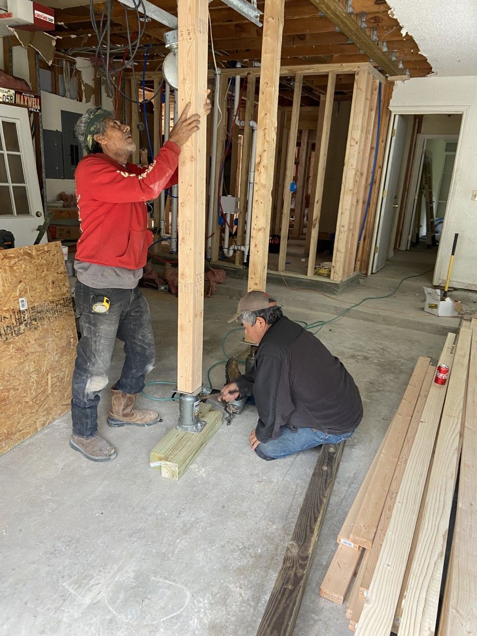 Two men constructing wooden support posts in a room; interior construction scene.