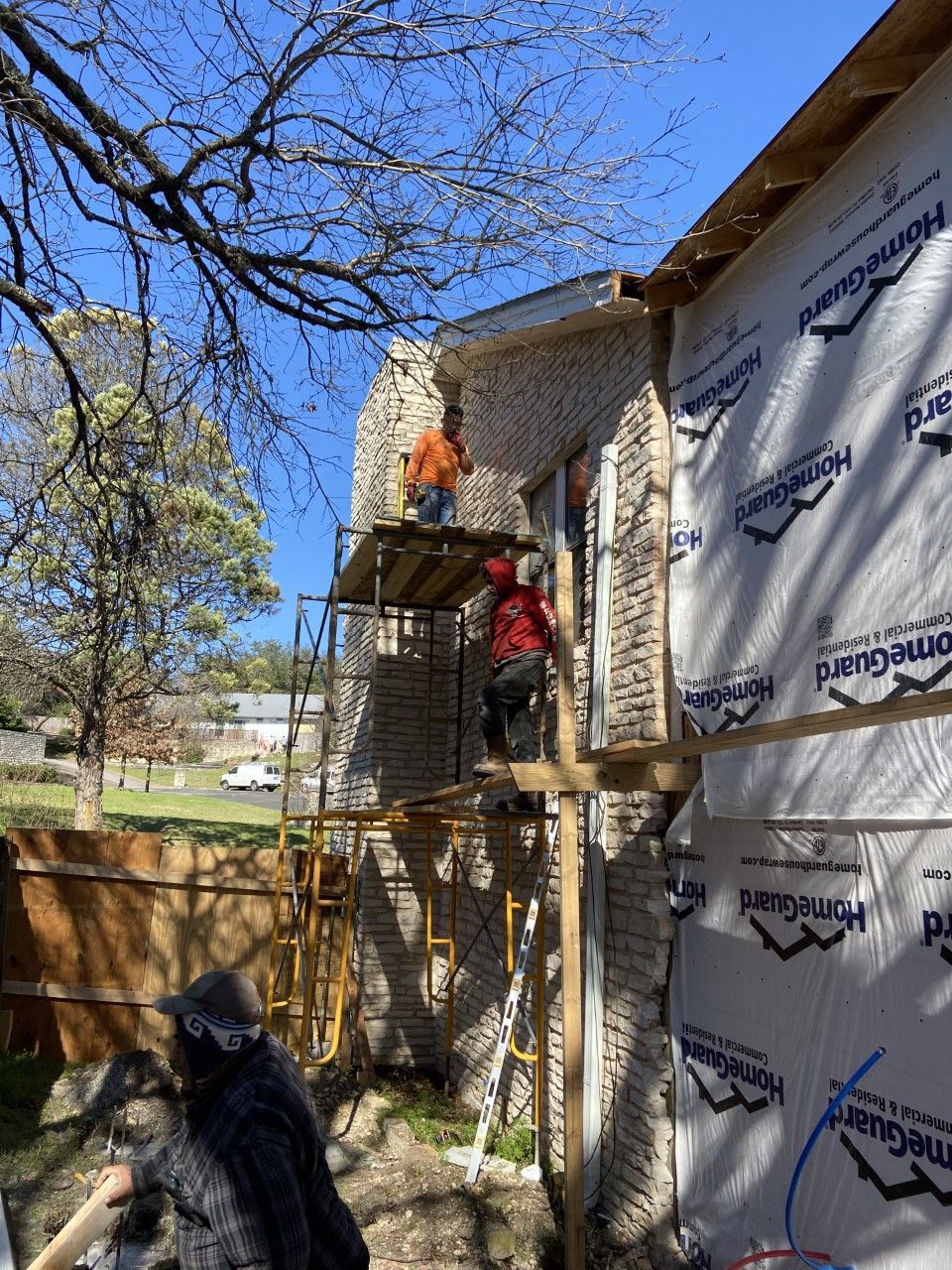 Construction workers adding stone to a house exterior. One is on scaffolding, one on the ground.