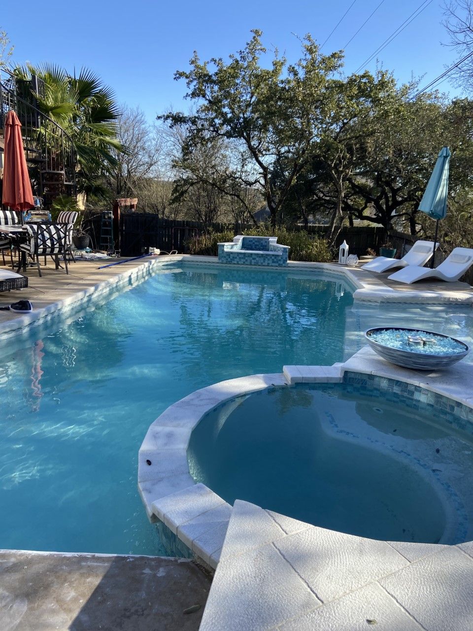 Swimming pool with spa and lounge chairs outdoors. Bright blue water, sunny day.