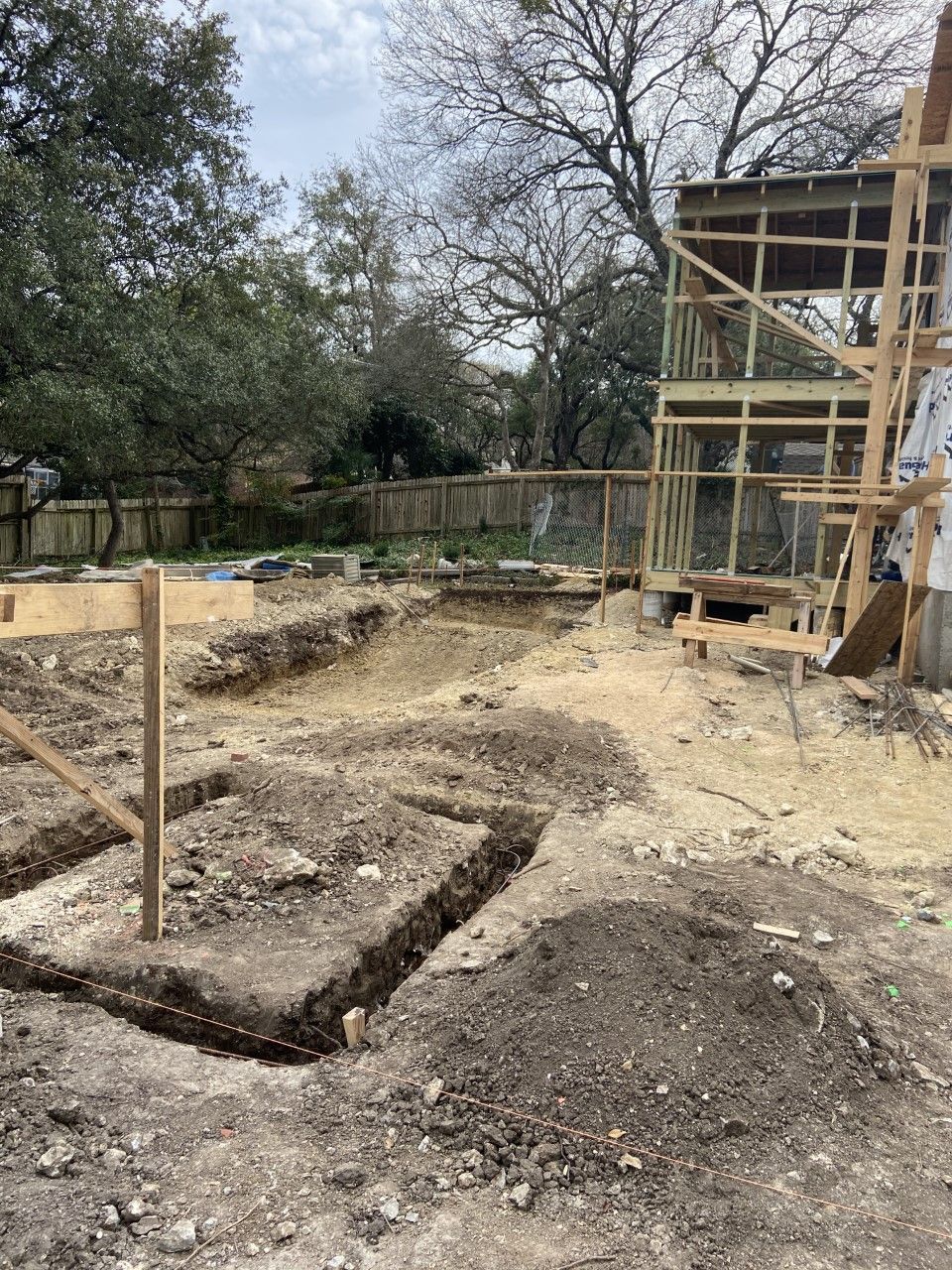Construction site with excavated trenches and wooden frame of a two-story building under construction.