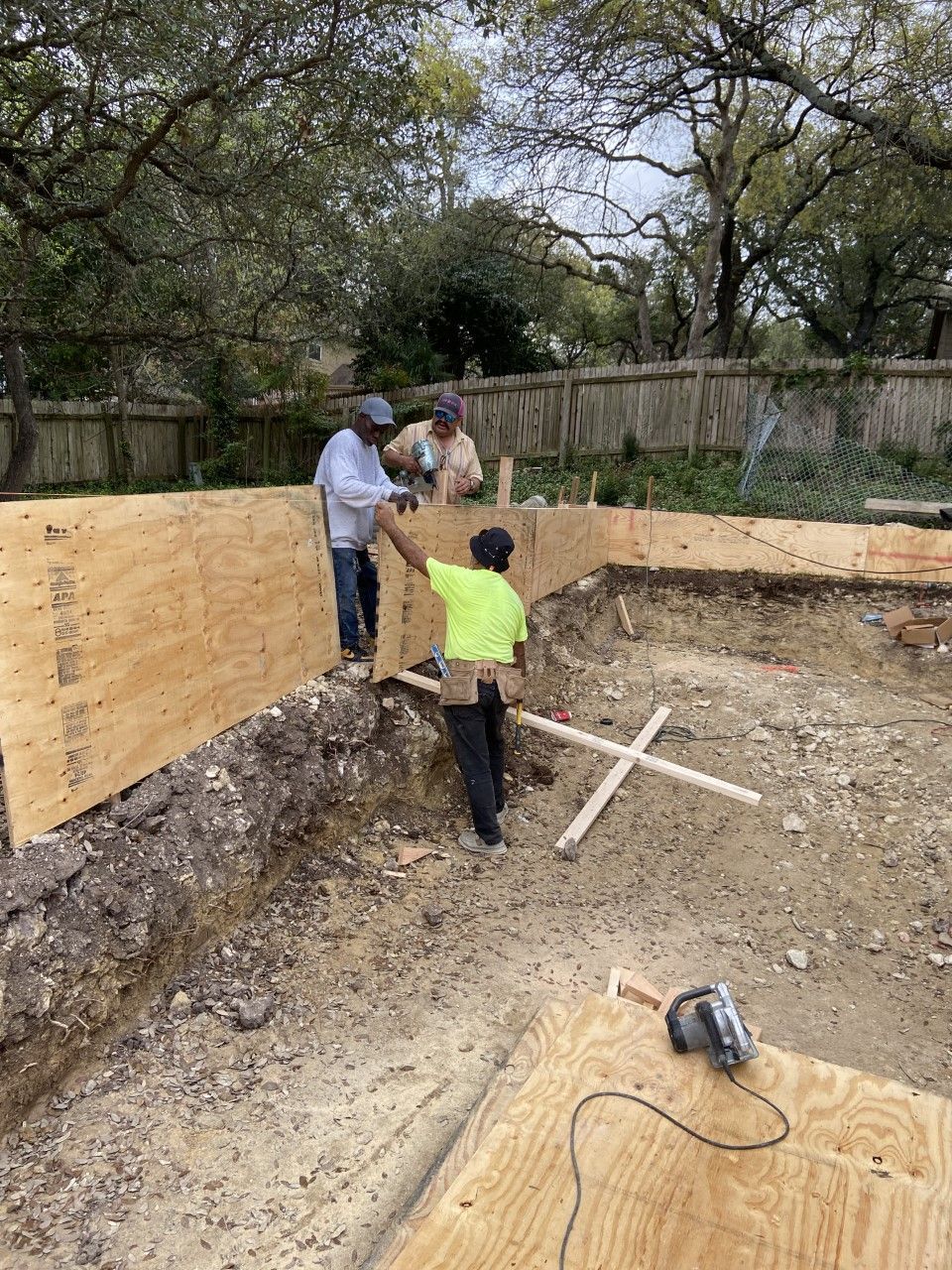 Construction workers building a wooden foundation. One in yellow shirt points as others work with wood.
