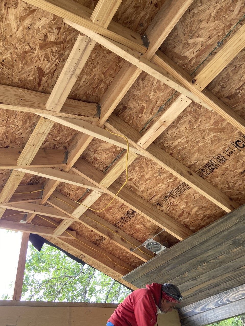 Wooden roof framing with curved beams, construction in progress. Person in red jacket is working below.