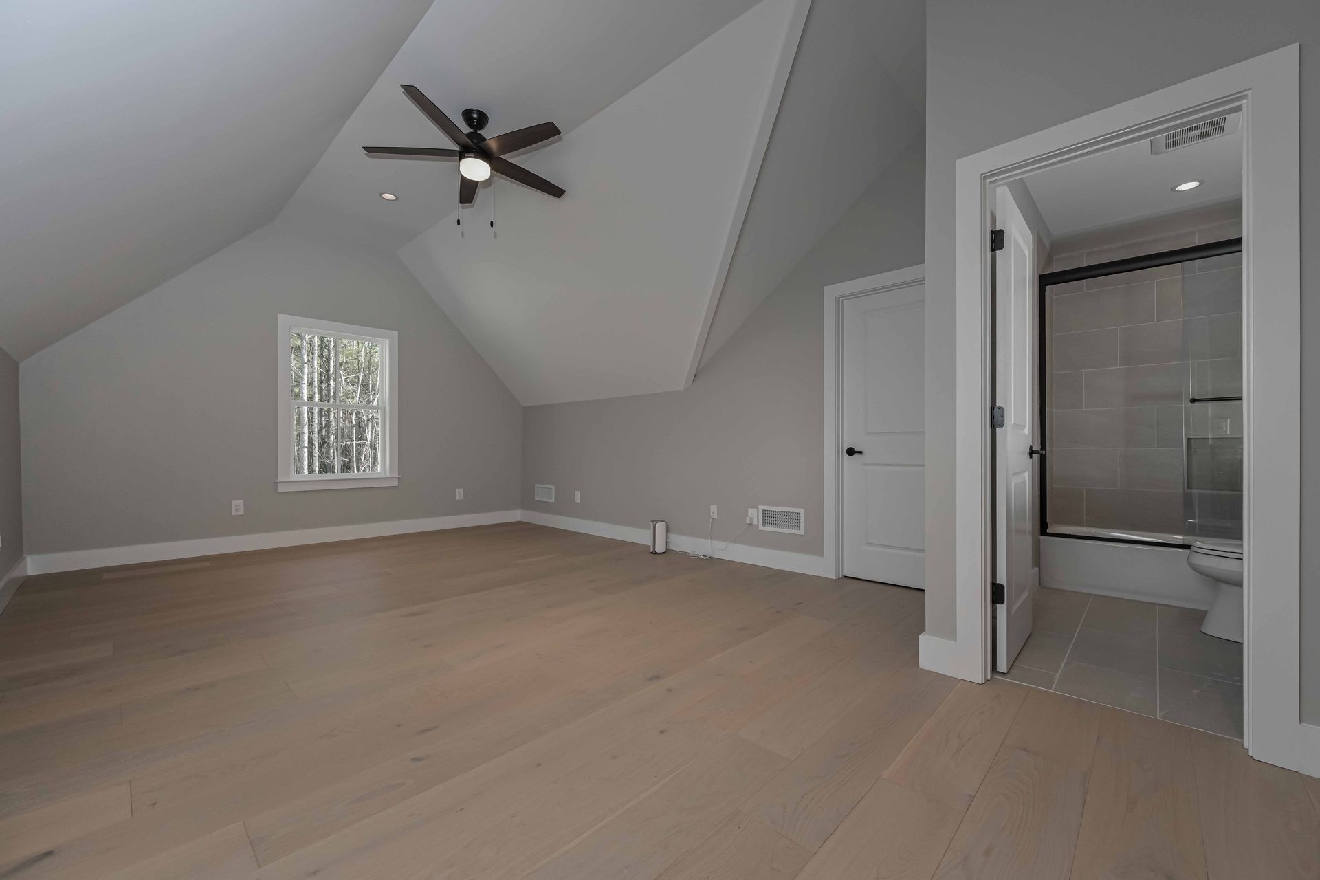 An empty bedroom with a ceiling fan and a bathroom.