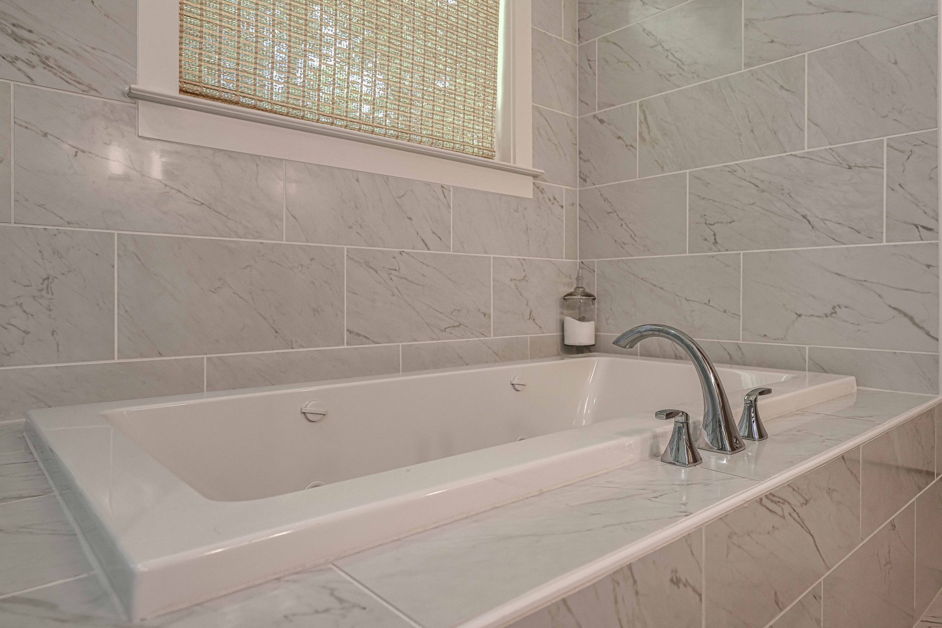 A bathtub in a bathroom with marble tiles and a window.
