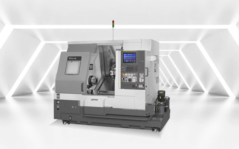 Tornio CNC, grigio e bianco, con pannello di controllo e luci di sicurezza, posizionato in una stanza bianca e luminosa.