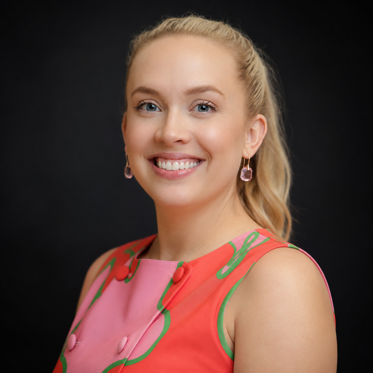 Smiling person in a coral dress against a dark studio background