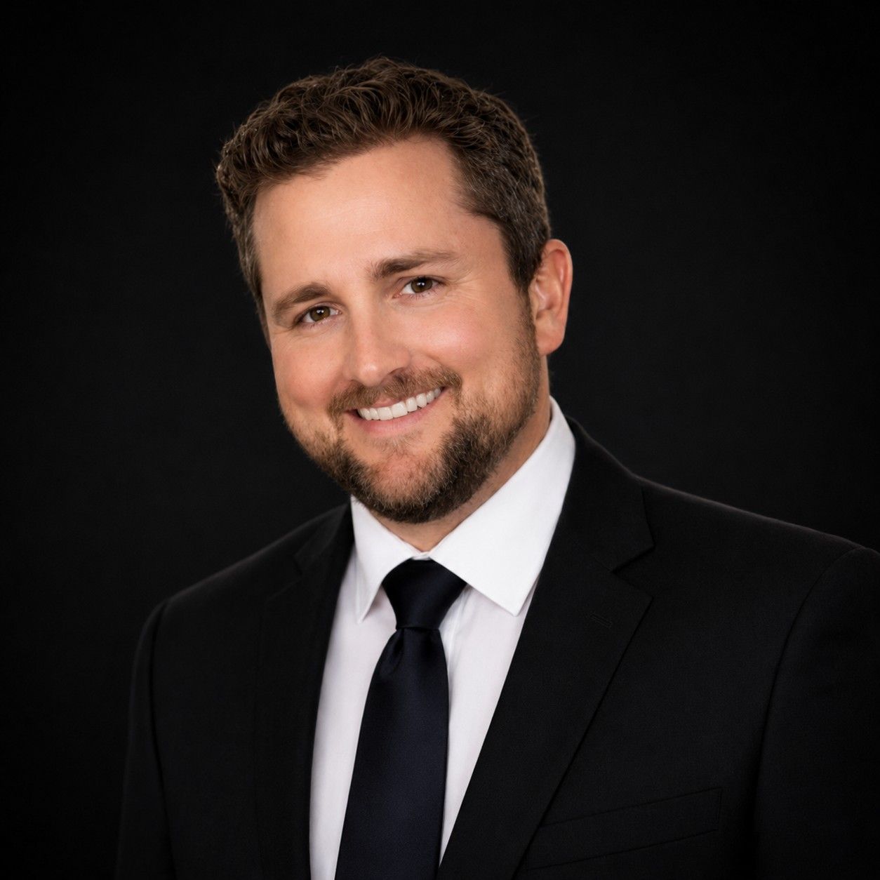 Smiling man in a black suit and tie against a dark background