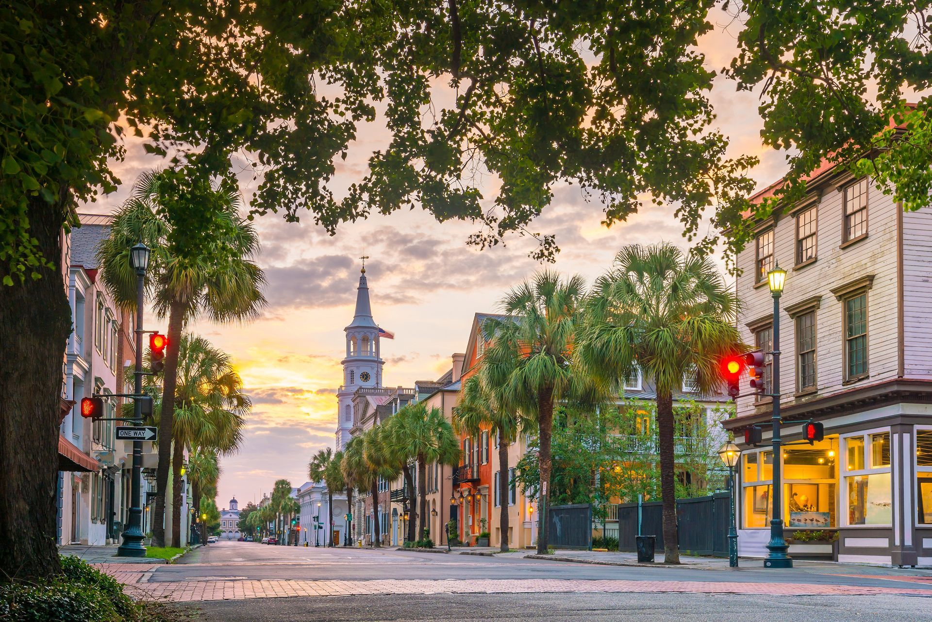 Empty cobblestone street at sunrise, lined with palm trees and historic buildings, with a church tower in the distance