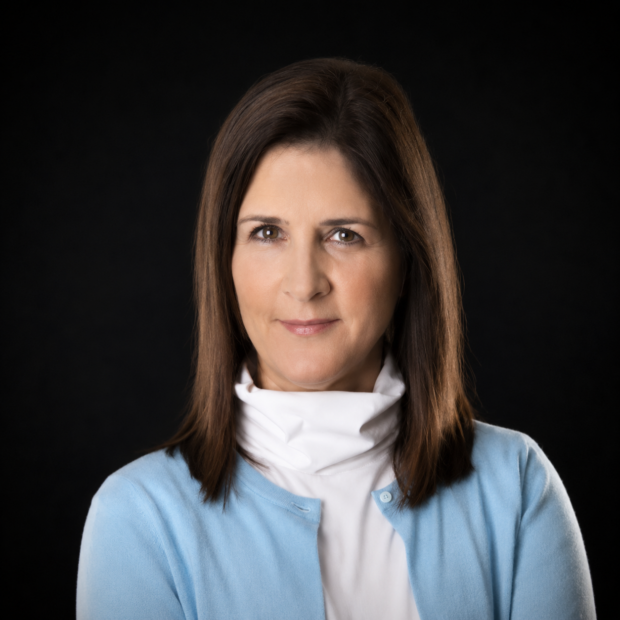 Studio portrait of a woman with brown hair wearing a light blue cardigan and white scarf against a dark background