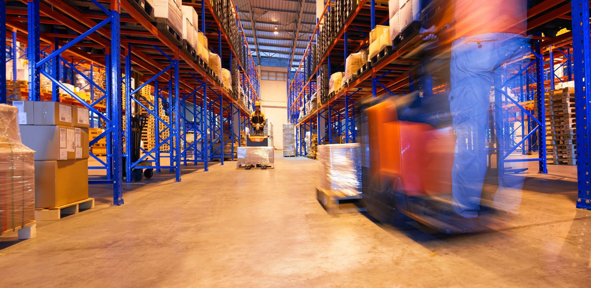 Warehouse interior with forklift in motion, loading goods from shelves stacked with boxes.