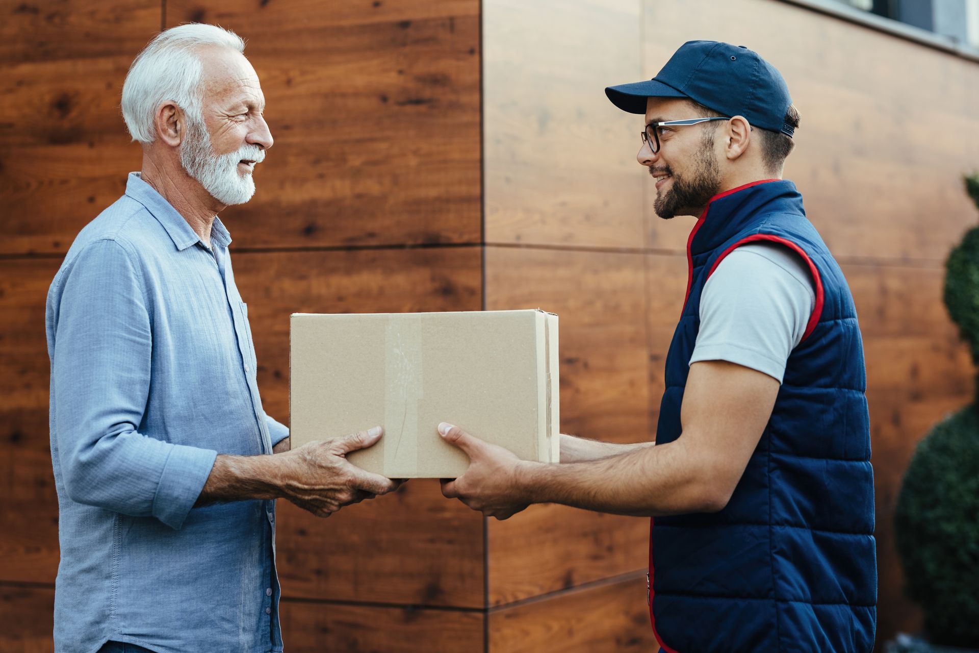 Delivery person hands a cardboard box to a man at a doorway.