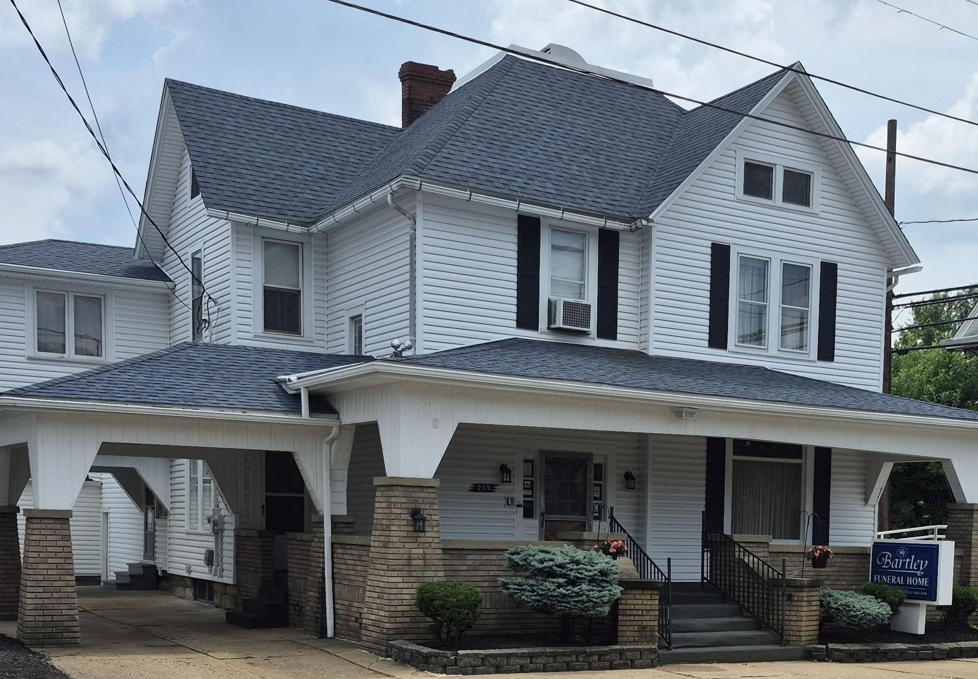 White two-story house with dark blue roof, black shutters, and a porch supported by stone columns.
