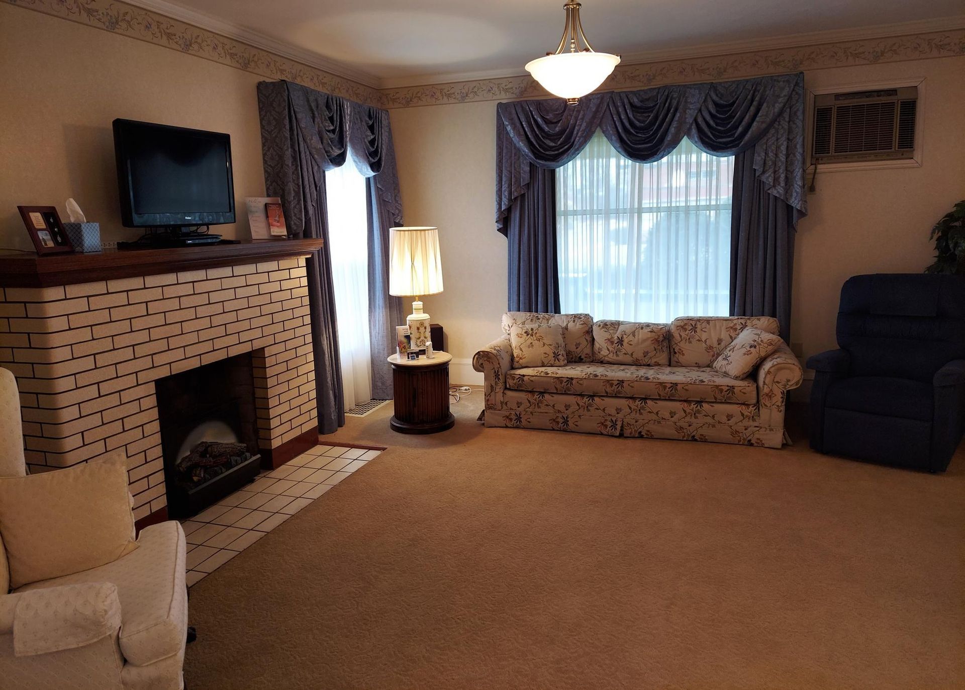 Living room with brick fireplace, sofa, and blue curtains. Beige carpet and off-white walls.