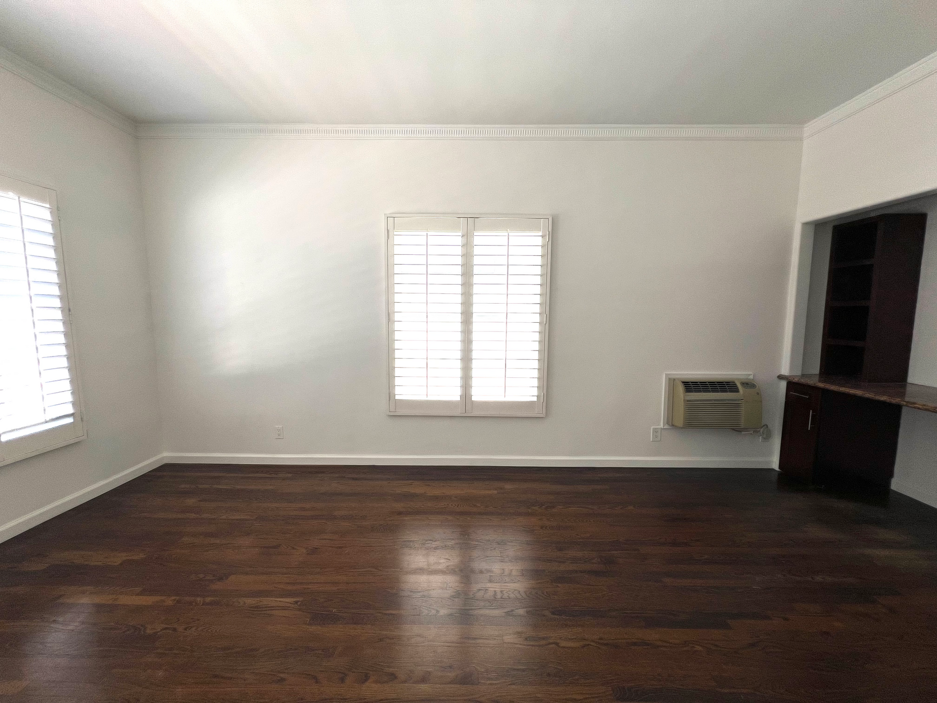An empty living room with hardwood floors and two windows.