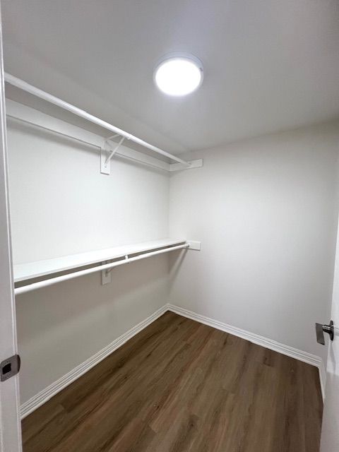 A walk in closet with hardwood floors and a light on the ceiling.